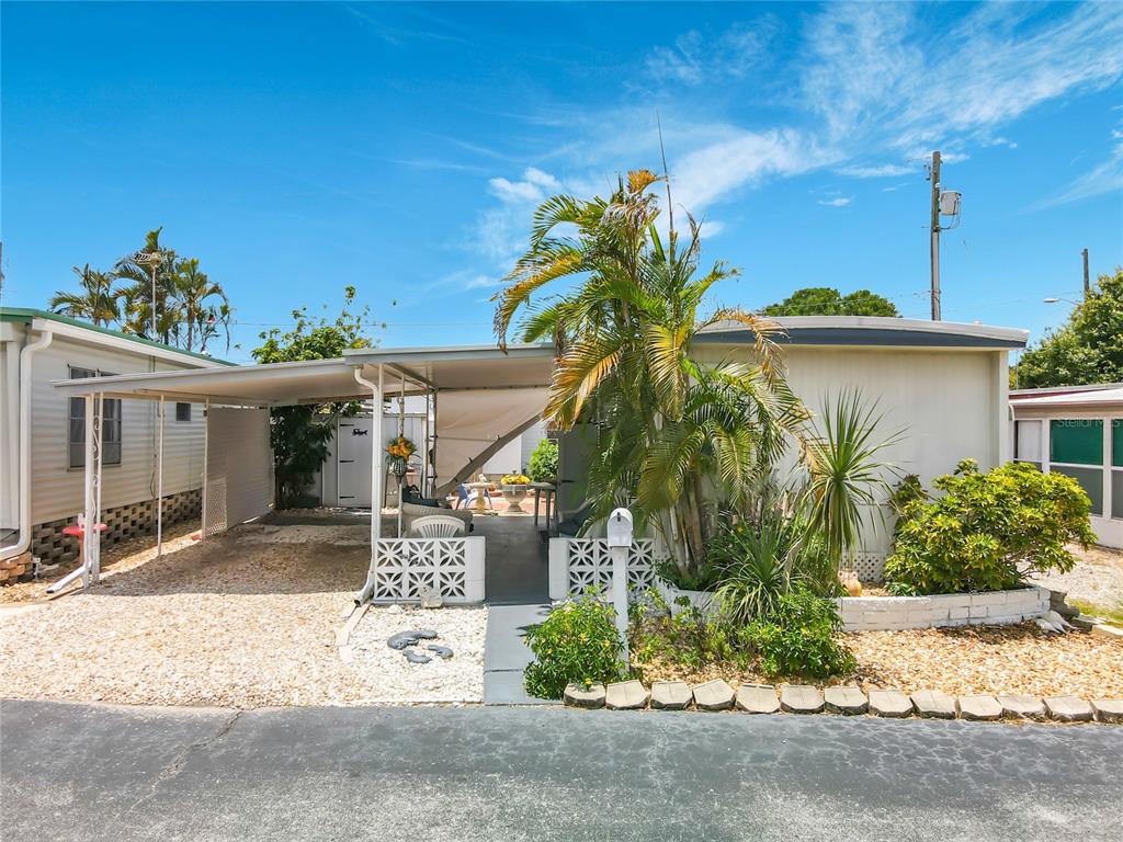 A single-story mobile home features a covered carport, a small patio, and tropical landscaping — 7490 46TH AVENUE N UNIT 109, ST PETERSBURG, FL