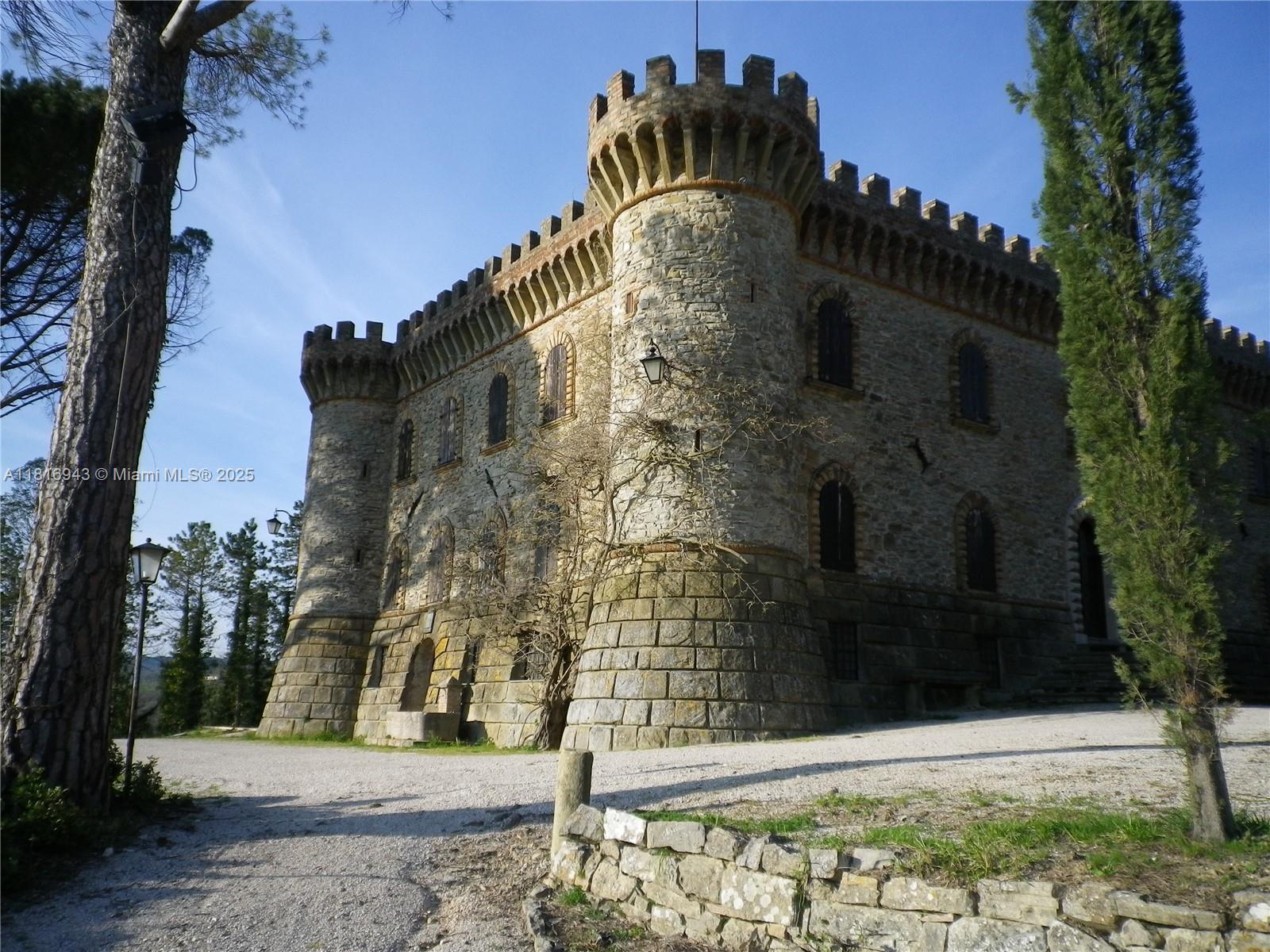 A stone castle exterior features corner towers, crenellated battlements, and arched windows under a blue sky — Assisi Frazione S. Gregorio, 0, 0