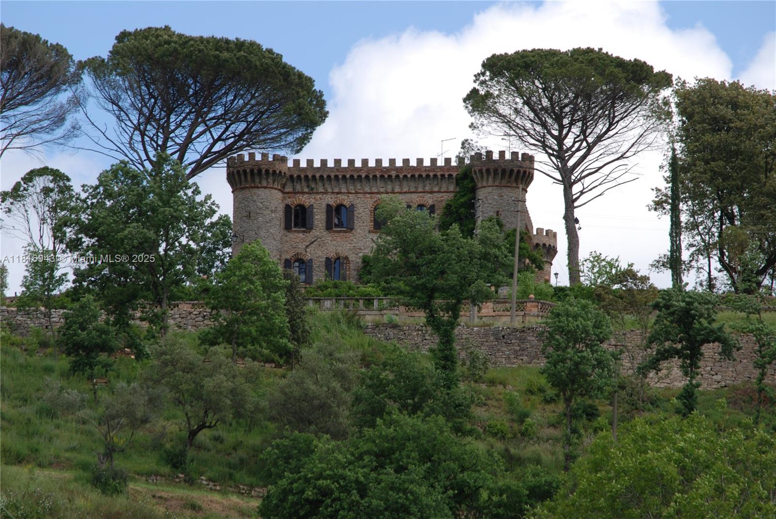 A stone castle with crenellated towers sits atop a hill surrounded by trees — Assisi Frazione S. Gregorio, 0, 0