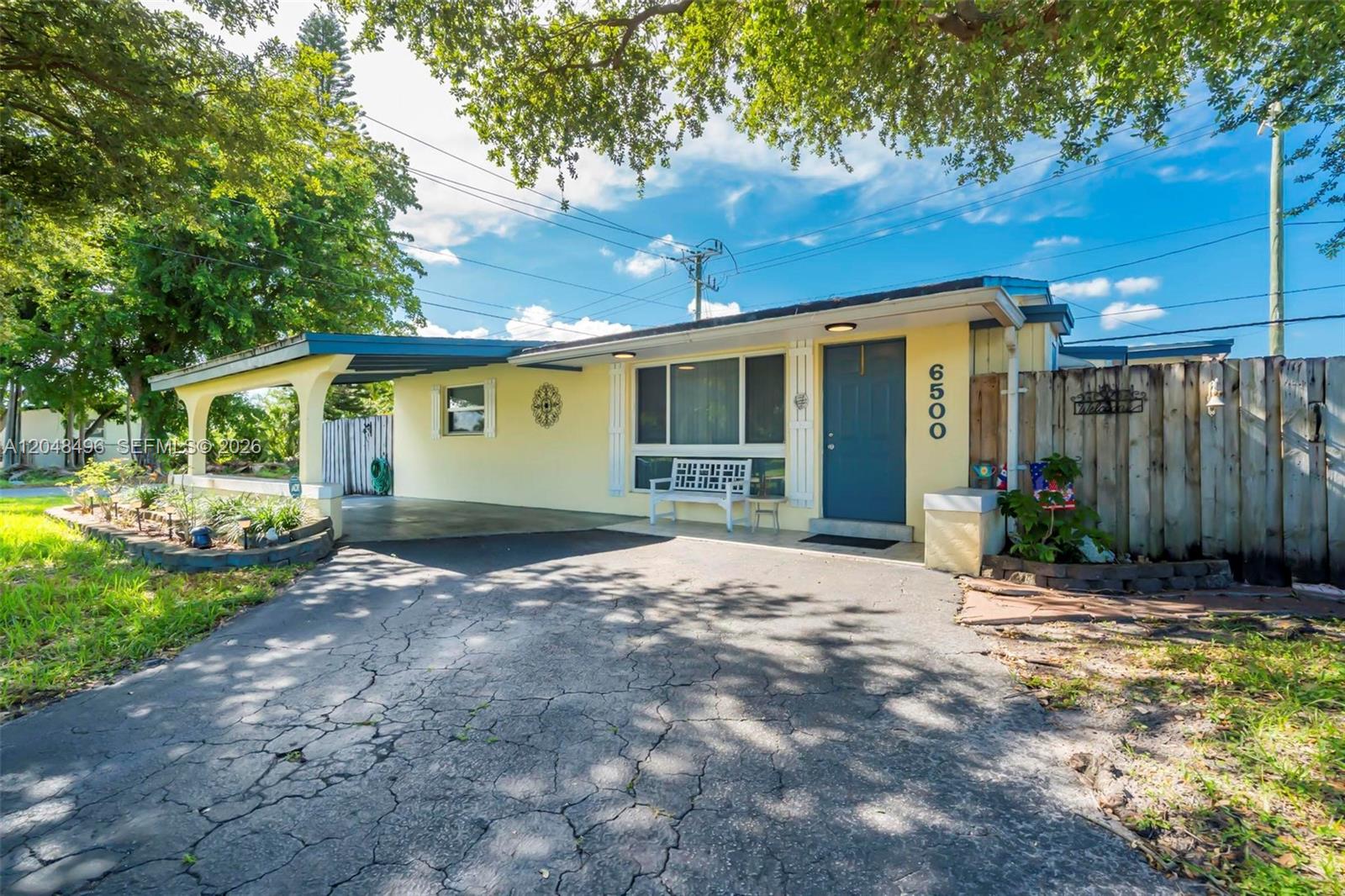 A yellow single-story house features a carport, a blue front door, and a paved driveway — 6500 Fletcher St, Hollywood FL 33023, HOLLYWOOD, FL
