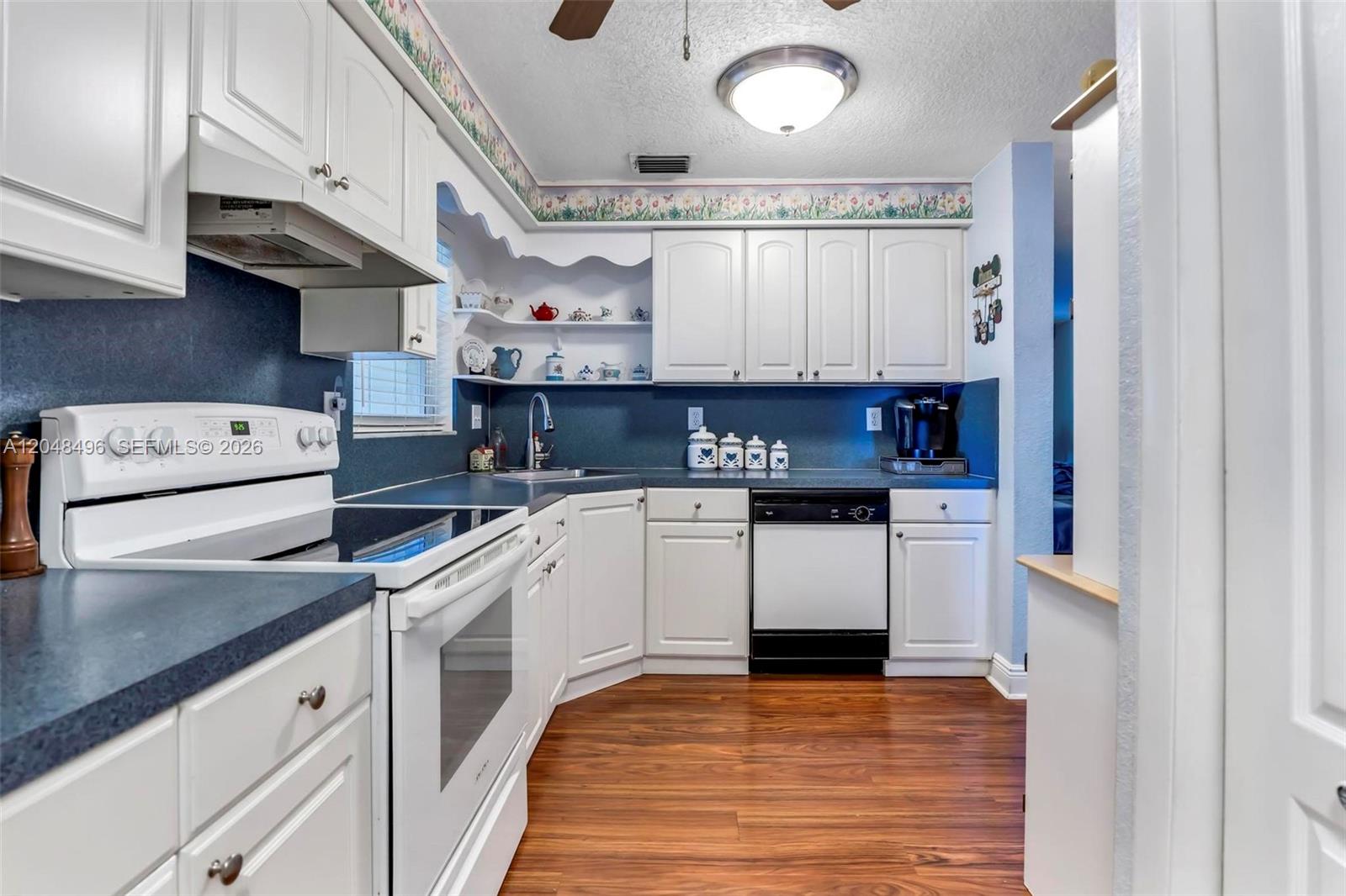 A kitchen features white cabinets, dark blue countertops, a white stove, and wood-look flooring — 6500 Fletcher St, Hollywood FL 33023, HOLLYWOOD, FL