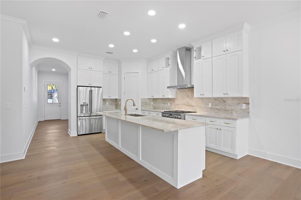 A modern white kitchen features a large island, stainless steel appliances, and light wood flooring — 4316 S RENELLIE DRIVE, TAMPA, FL