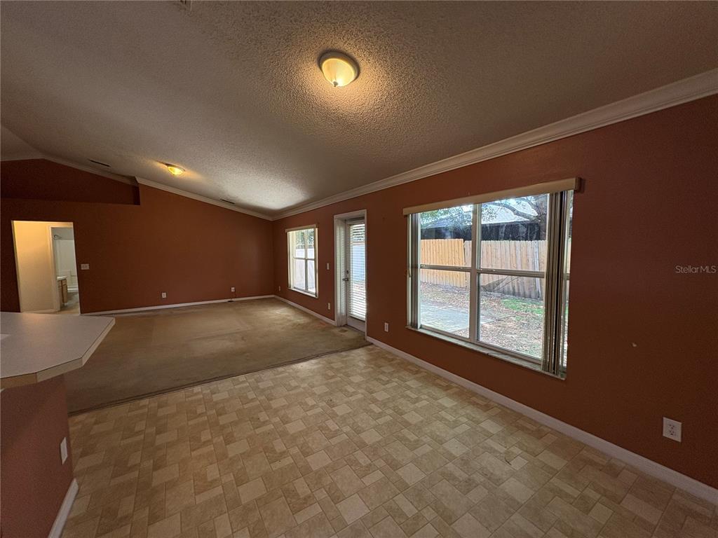 An open-concept living and dining area features terracotta walls, carpeted flooring, and a sliding door — 104 HERRING LANE, POINCIANA, FL