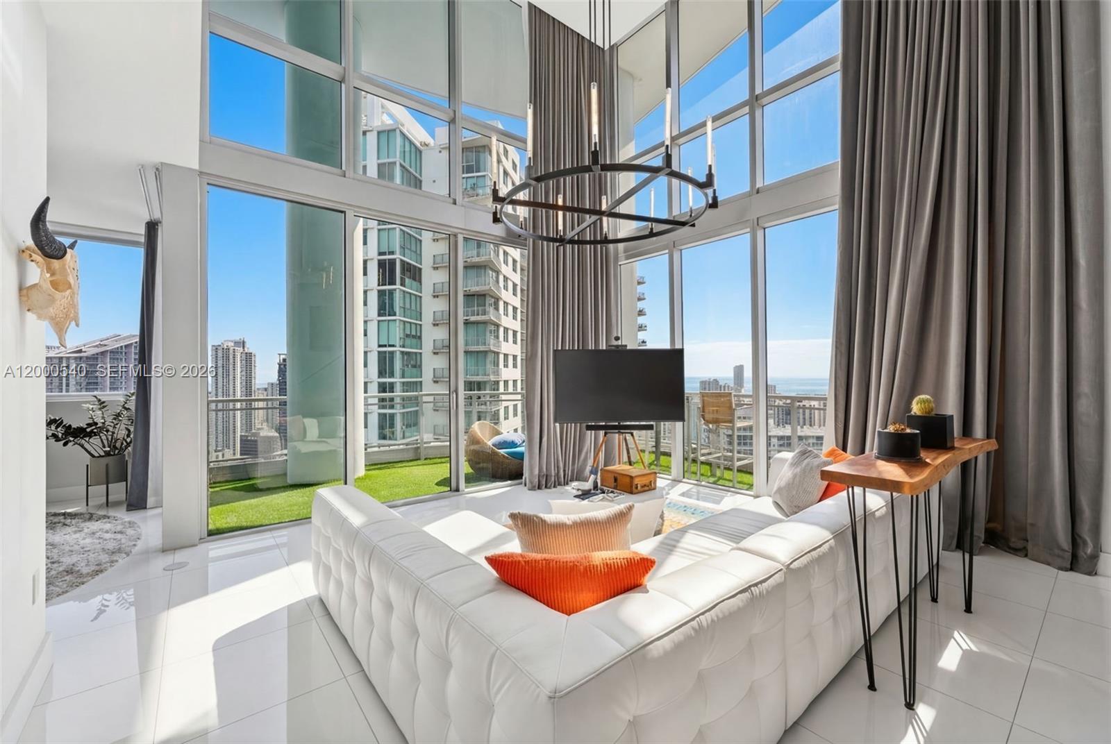A modern living room features floor-to-ceiling windows, a white tufted sofa, and a balcony view — 90 SW 3rd St # 12, Miami FL 33130, MIAMI, FL