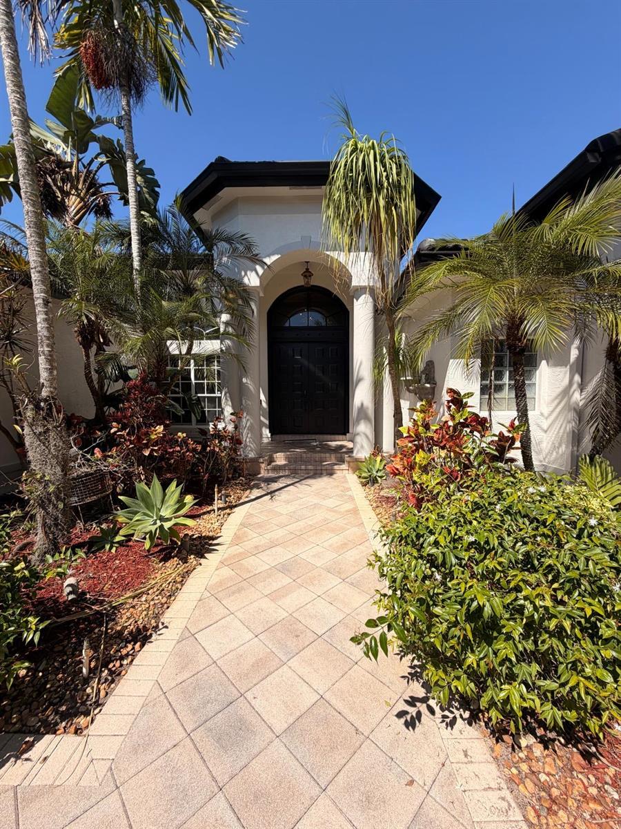 A paved walkway leads to the arched entryway of a house with tropical landscaping — 3309 Bradenham Lane, Davie FL 33328, DAVIE, FL