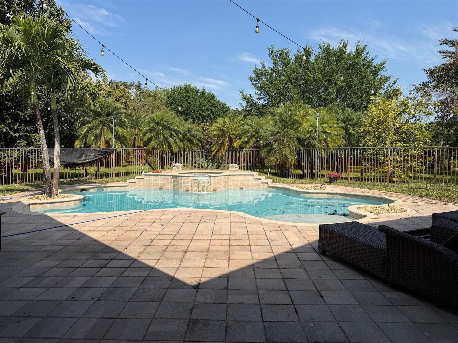 A backyard swimming pool with a raised spa and waterfall, surrounded by a paved patio — 3309 Bradenham Lane, Davie FL 33328, DAVIE, FL
