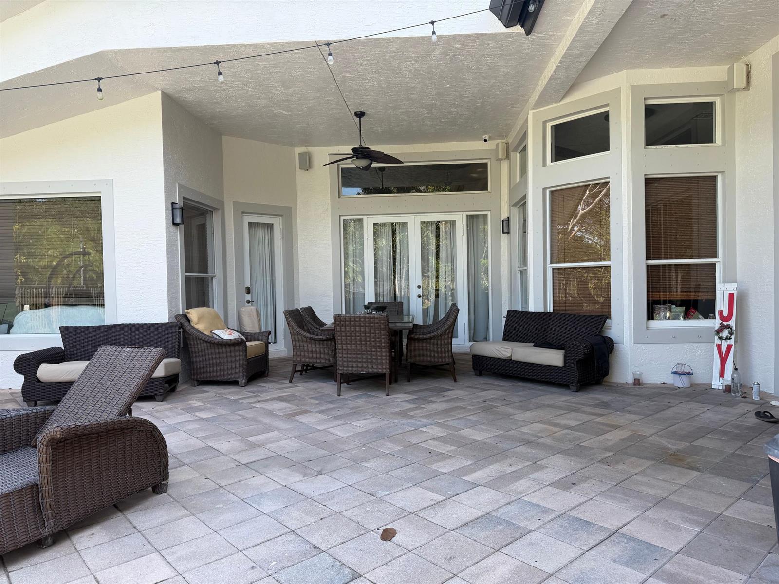A covered outdoor patio features wicker furniture, a dining set, and light-colored stone pavers — 3309 Bradenham Lane, Davie FL 33328, DAVIE, FL