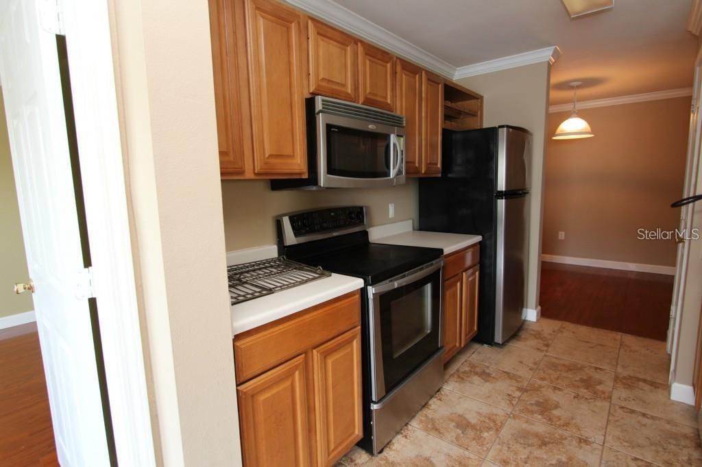 A kitchen features wood cabinets, stainless steel appliances, and light-colored tile flooring — 18517 BRIDLE CLUB DRIVE UNIT 18517, TAMPA, FL