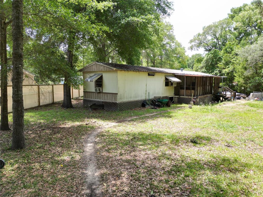 A single-wide mobile home with a screened-in porch sits on a grassy, tree-shaded lot — 4667 NE 140TH COURT, WILLISTON, FL