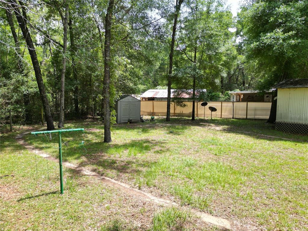 A grassy backyard features a clothesline, a small storage shed, and a privacy fence — 4667 NE 140TH COURT, WILLISTON, FL