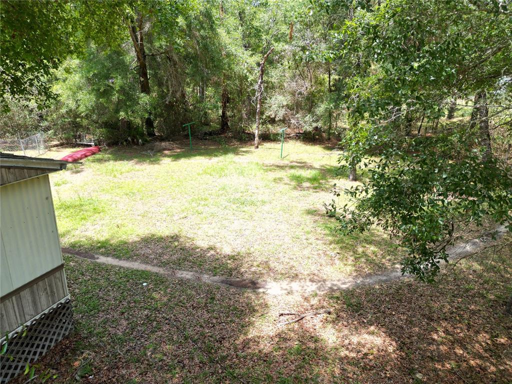 A grassy backyard area with trees and a portion of a mobile home exterior — 4667 NE 140TH COURT, WILLISTON, FL