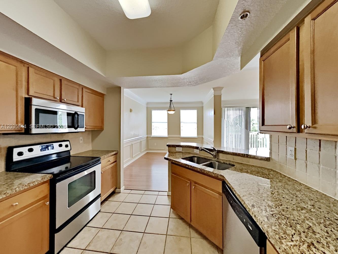 A kitchen with wood cabinets, granite countertops, and stainless steel appliances overlooks a dining area — JUPITER, FL