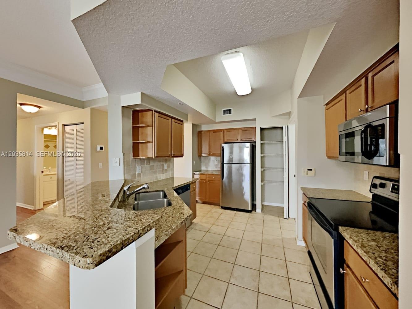 A kitchen features wood cabinets, granite countertops, stainless steel appliances, and tile flooring — JUPITER, FL