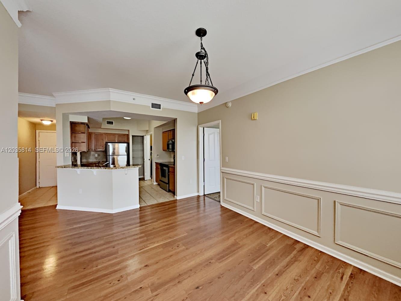 A dining area with wood flooring, wainscoting, and a pendant light overlooks an open kitchen — JUPITER, FL