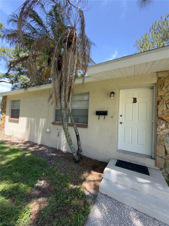 Exterior view of a single-story building with a white door marked B and a palm tree — 7746 62ND STREET N UNIT B, PINELLAS PARK, FL
