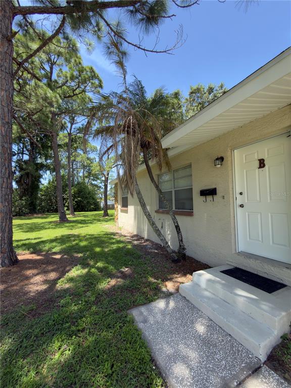 Exterior view of a beige stucco building with a white door labeled B and palm trees — 7746 62ND STREET N UNIT B, PINELLAS PARK, FL