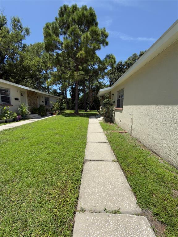 A concrete walkway runs between two single-story residential buildings with a grassy lawn and trees — 7746 62ND STREET N UNIT B, PINELLAS PARK, FL
