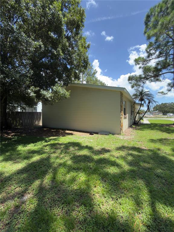 The side exterior of a light-colored house features a stone accent wall and surrounding trees — 7746 62ND STREET N UNIT B, PINELLAS PARK, FL
