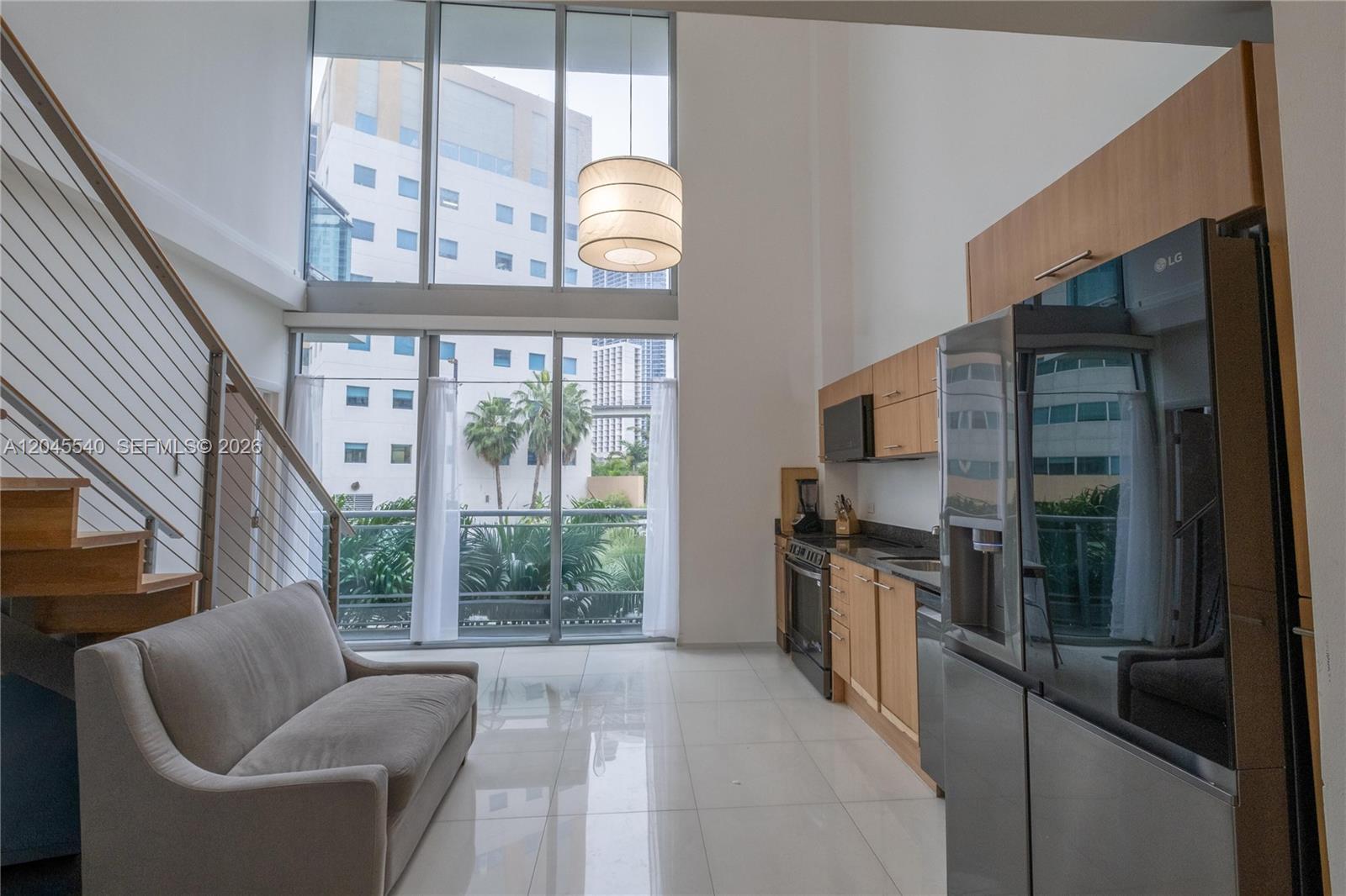 A modern living room and kitchen area features high ceilings, floor-to-ceiling windows, and tile flooring — 350 S Miami Ave # 306, Miami FL 33130, MIAMI, FL