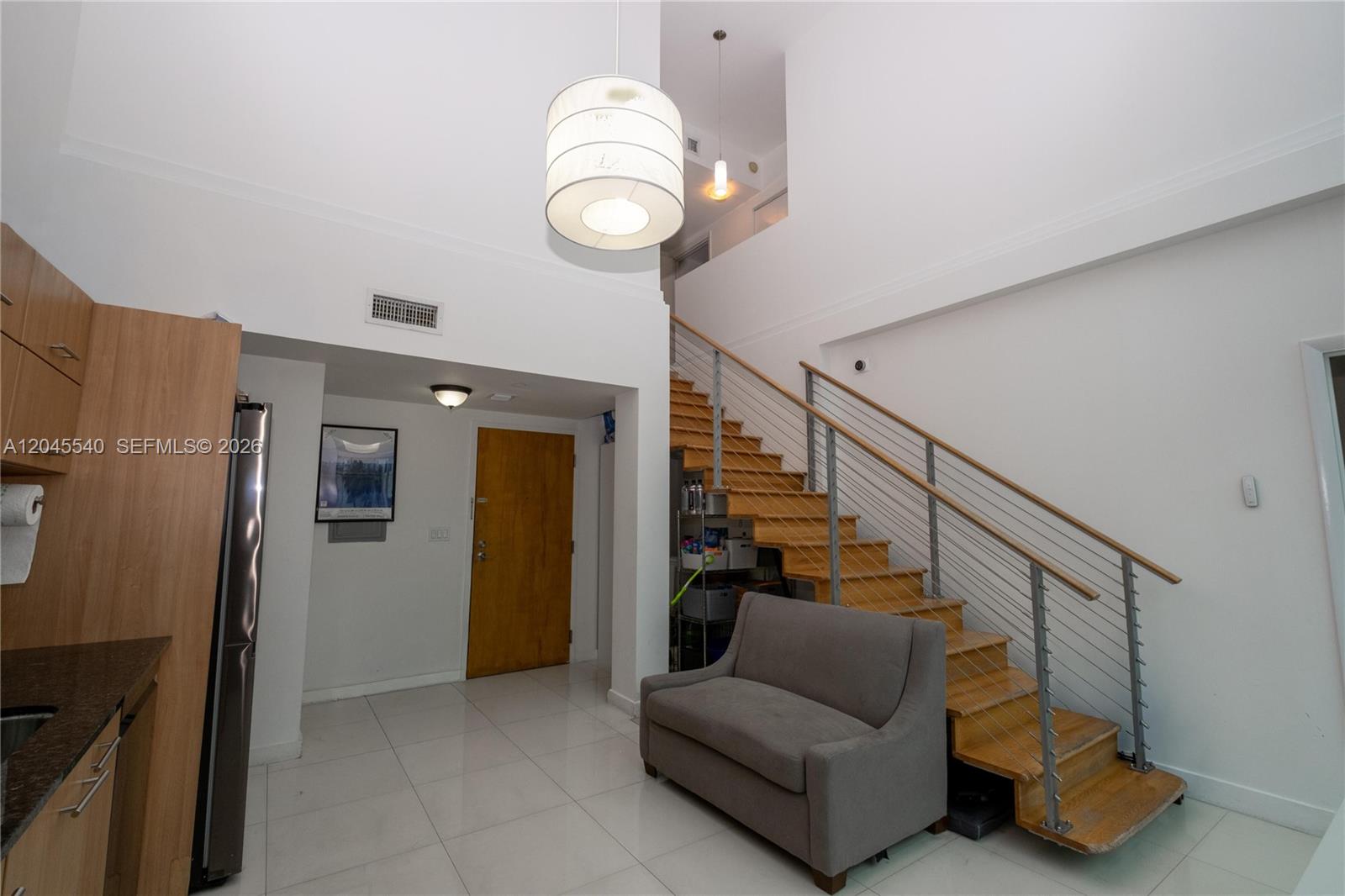 A modern living area features a wooden staircase, a grey sofa, and high ceilings — 350 S Miami Ave # 306, Miami FL 33130, MIAMI, FL