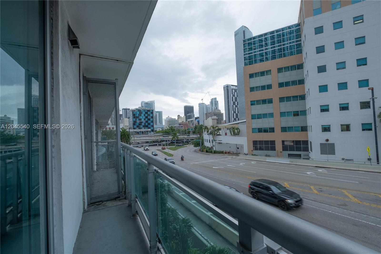 A balcony overlooks a city street with traffic and surrounding high-rise buildings — 350 S Miami Ave # 306, Miami FL 33130, MIAMI, FL