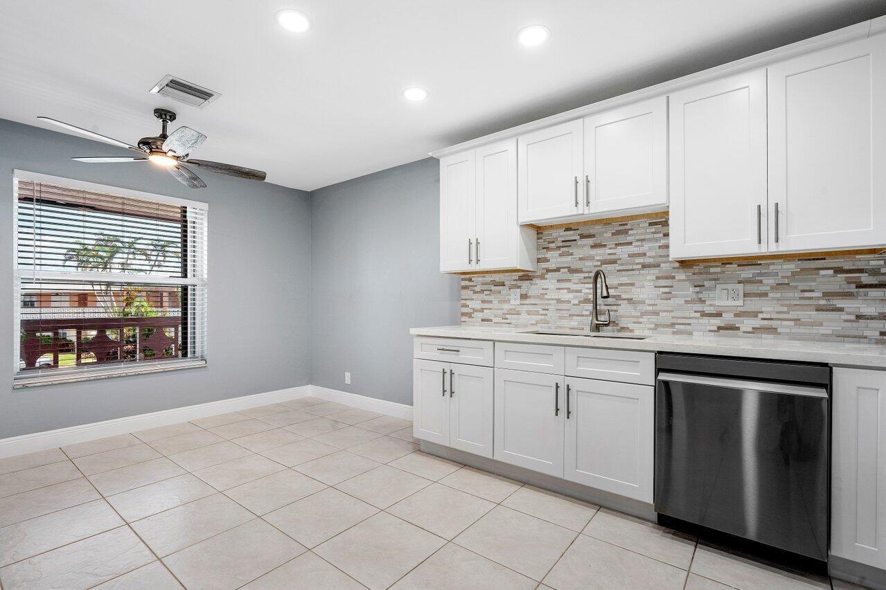 A kitchen features white cabinets, a mosaic tile backsplash, stainless steel appliances, and tile flooring — 1740 NW 19th Terrace # 204, Delray Beach FL 33445, DELRAY BEACH, FL