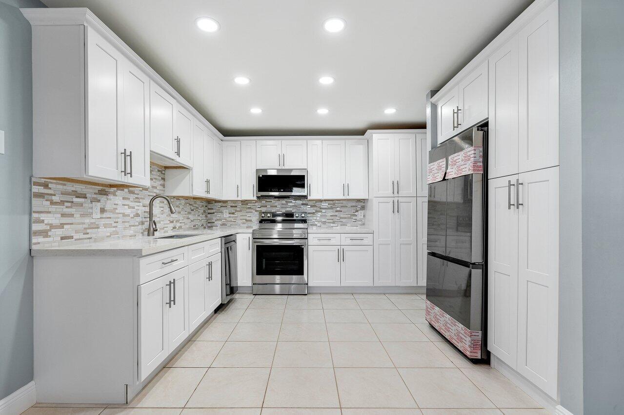 A modern kitchen features white shaker cabinets, stainless steel appliances, and a tiled backsplash — 1740 NW 19th Terrace # 204, Delray Beach FL 33445, DELRAY BEACH, FL