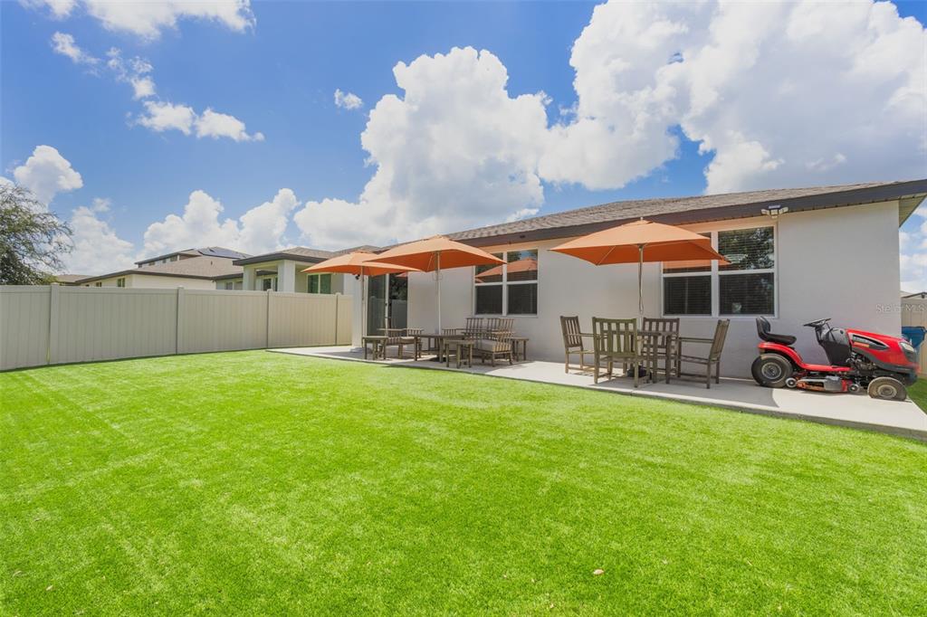 A backyard with a concrete patio, two orange umbrellas, outdoor furniture, and a riding lawnmower — 840 TETON STREET, HAINES CITY, FL