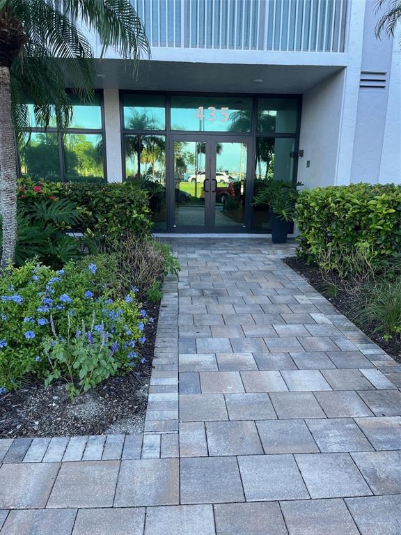 A paved walkway leads to the glass-paned entrance of a building marked with the number 435 — 435 S GULFSTREAM AVENUE UNIT 206, SARASOTA, FL