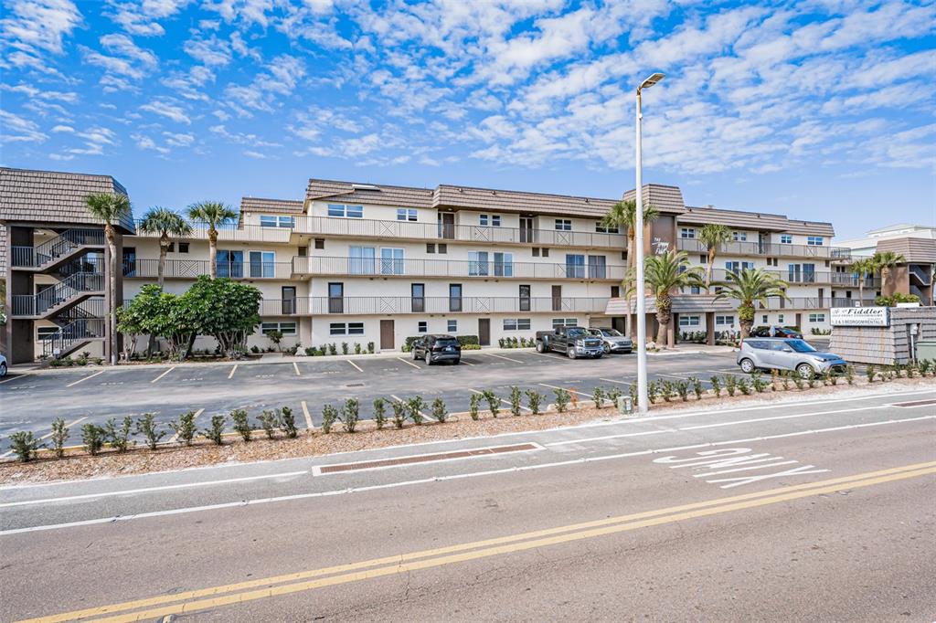 A multi-story apartment building with a parking lot and palm trees under a blue sky — 60 GULF BOULEVARD UNIT 203, INDIAN ROCKS BEACH, FL
