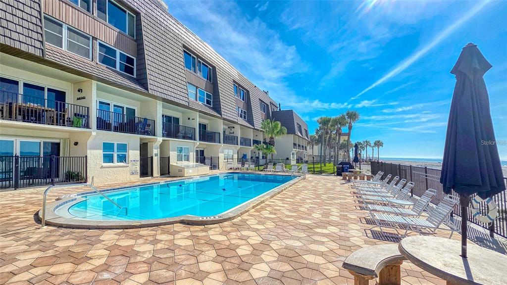 A swimming pool sits on a paved patio beside a multi-story building near the beach — 60 GULF BOULEVARD UNIT 203, INDIAN ROCKS BEACH, FL