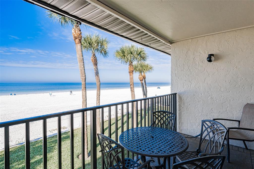 A balcony with patio furniture overlooks a sandy beach and the ocean with palm trees — 60 GULF BOULEVARD UNIT 203, INDIAN ROCKS BEACH, FL