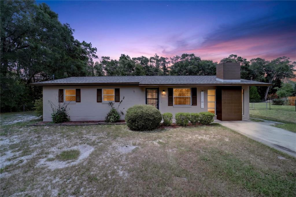 A single-story house with a beige exterior, a brown chimney, and a front lawn at dusk — 2875 NE 49TH STREET, OCALA, FL