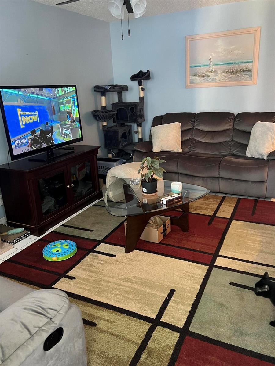 A living room features a dark sofa, a glass coffee table, and a television console — 3220 Holiday Springs Boulevard # 210, Margate FL 33063, MARGATE, FL