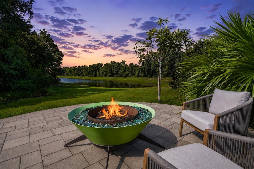 A patio with a green fire pit and chairs overlooks a lake at sunset — 30801 PARROT REEF COURT, WESLEY CHAPEL, FL