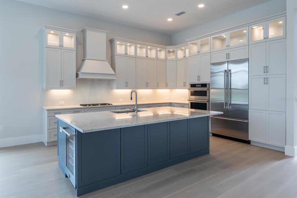 A modern kitchen features a dark blue island, light gray cabinetry, and stainless steel appliances — 257 BLUE PEARL CT., SARASOTA, FL