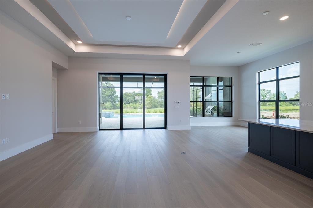 A bright living area with light wood floors, a tray ceiling, and large glass doors — 257 BLUE PEARL CT., SARASOTA, FL
