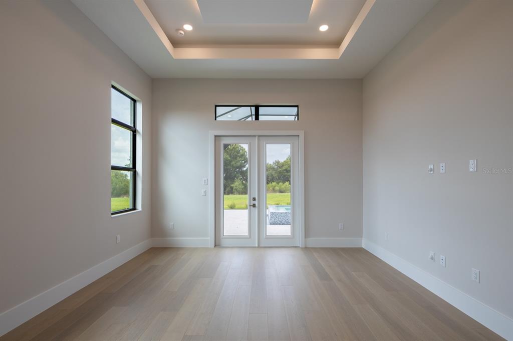 An empty room with light wood floors, a tray ceiling, and glass doors to a patio — 257 BLUE PEARL CT., SARASOTA, FL