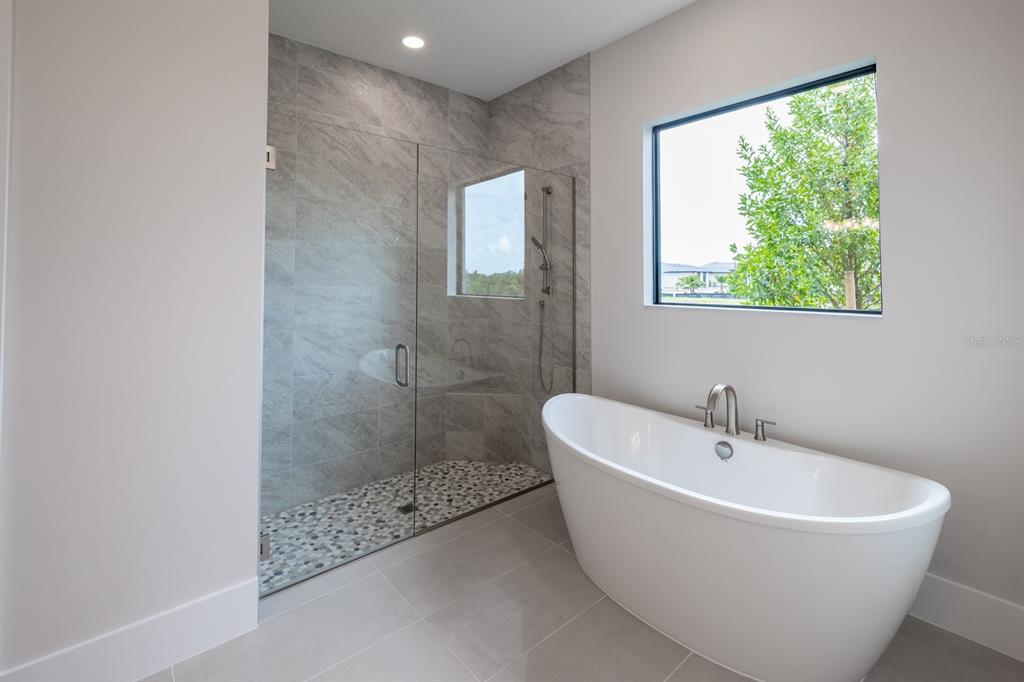 A modern bathroom features a freestanding white tub and a glass-enclosed shower with stone tile — 257 BLUE PEARL CT., SARASOTA, FL