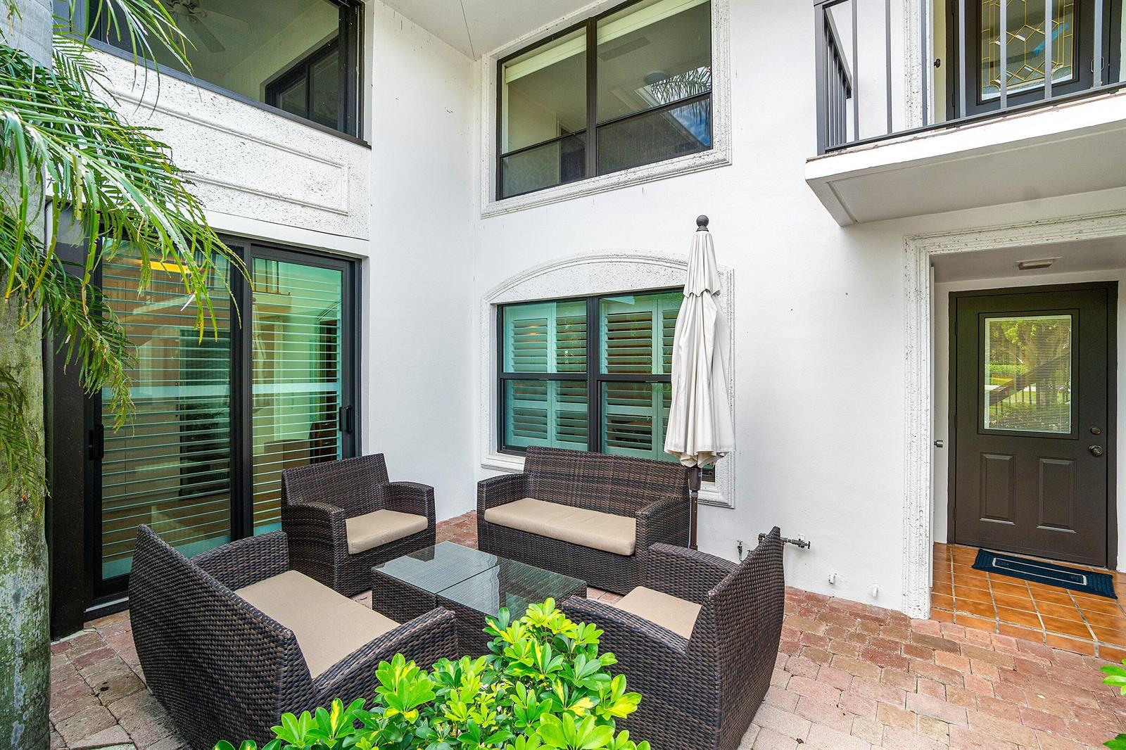 A paved courtyard features wicker patio furniture, a glass-topped table, and a closed patio umbrella — 3944 Quail Ridge Dr Drive N, Boynton Beach FL 33436, BOYNTON BEACH, FL