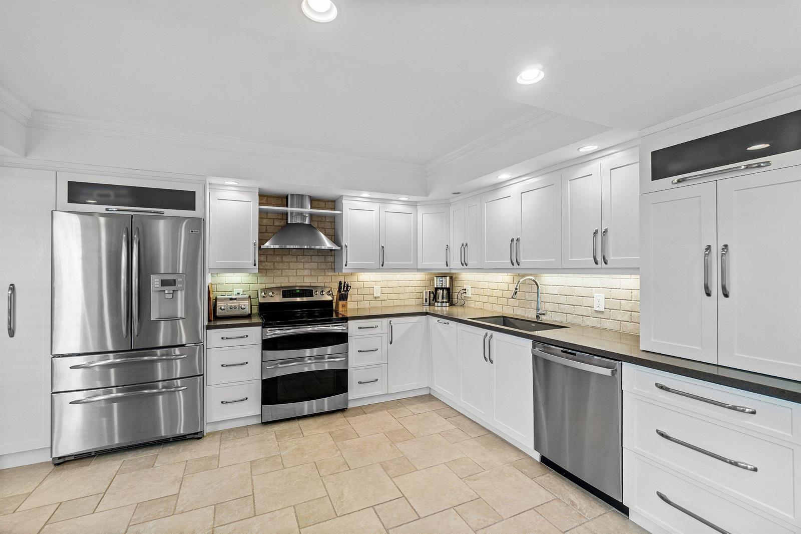 A kitchen features white cabinets, stainless steel appliances, a brick backsplash, and light tile flooring — 3944 Quail Ridge Dr Drive N, Boynton Beach FL 33436, BOYNTON BEACH, FL