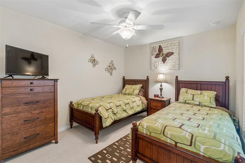 A bedroom features two twin beds with green patterned bedding, a dresser, and a ceiling fan — 6715 GRAND ESTUARY TRAIL UNIT 203, BRADENTON, FL
