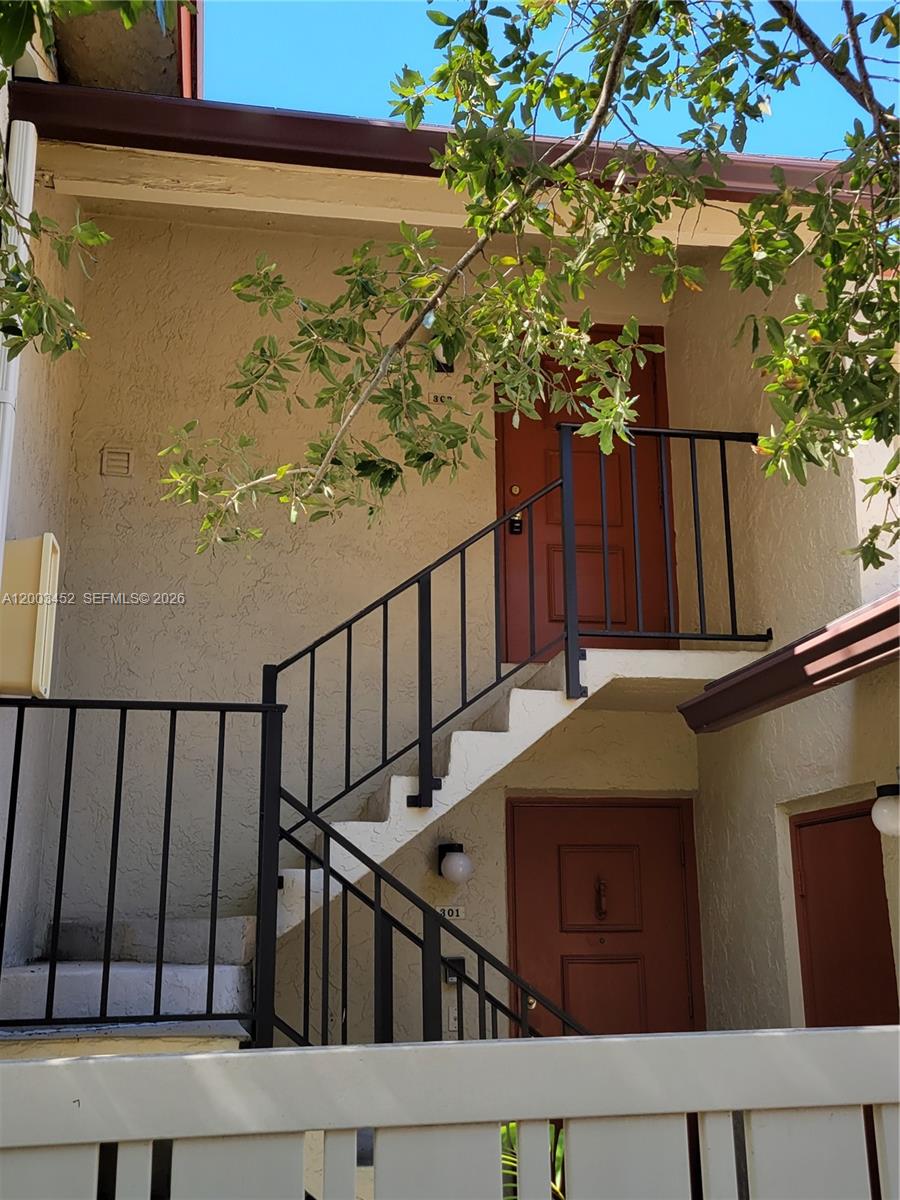 An exterior view shows a tan building with two red doors and a black metal staircase — 1821 NE 40th Ct # 302, Pompano Beach FL 33064, POMPANO BEACH, FL