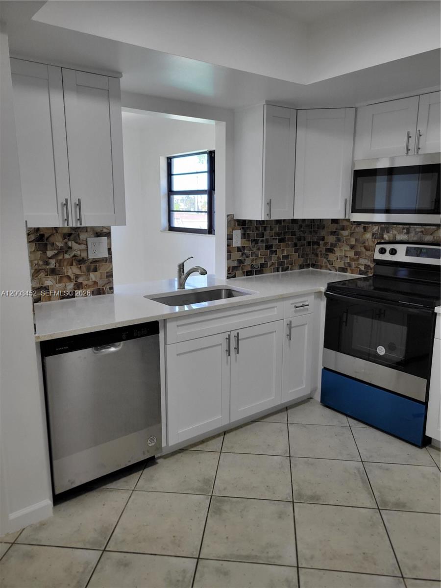 A kitchen features white cabinets, stainless steel appliances, a tiled backsplash, and light-colored countertops — 1821 NE 40th Ct # 302, Pompano Beach FL 33064, POMPANO BEACH, FL