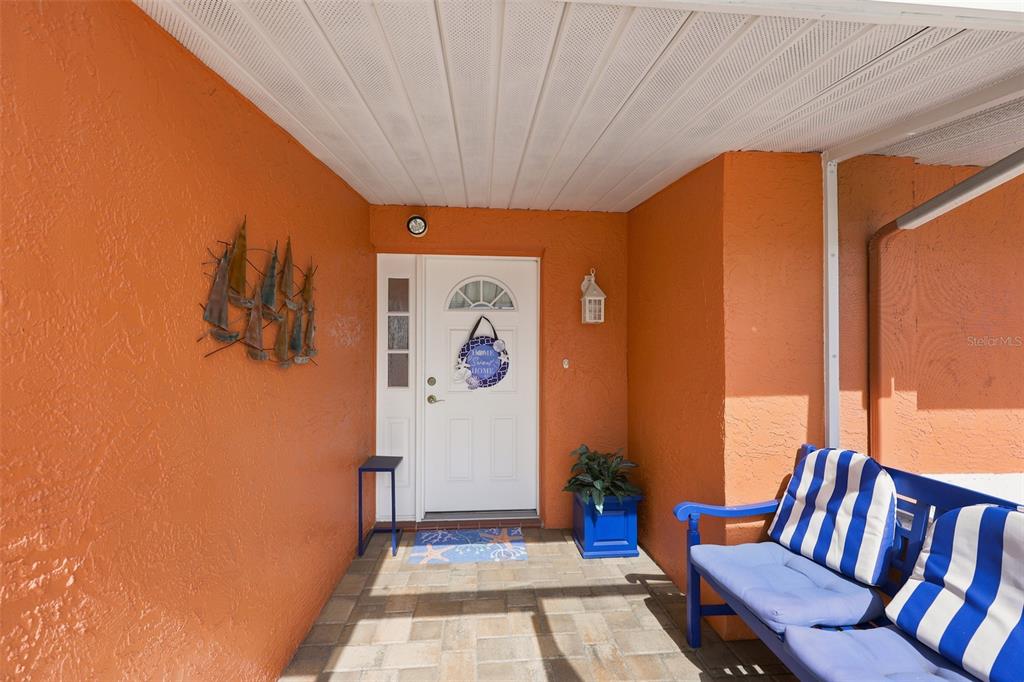 A covered front porch features orange stucco walls, a white door, and a blue bench — 1002 EL RANCHO DRIVE, SUN CITY CENTER, FL