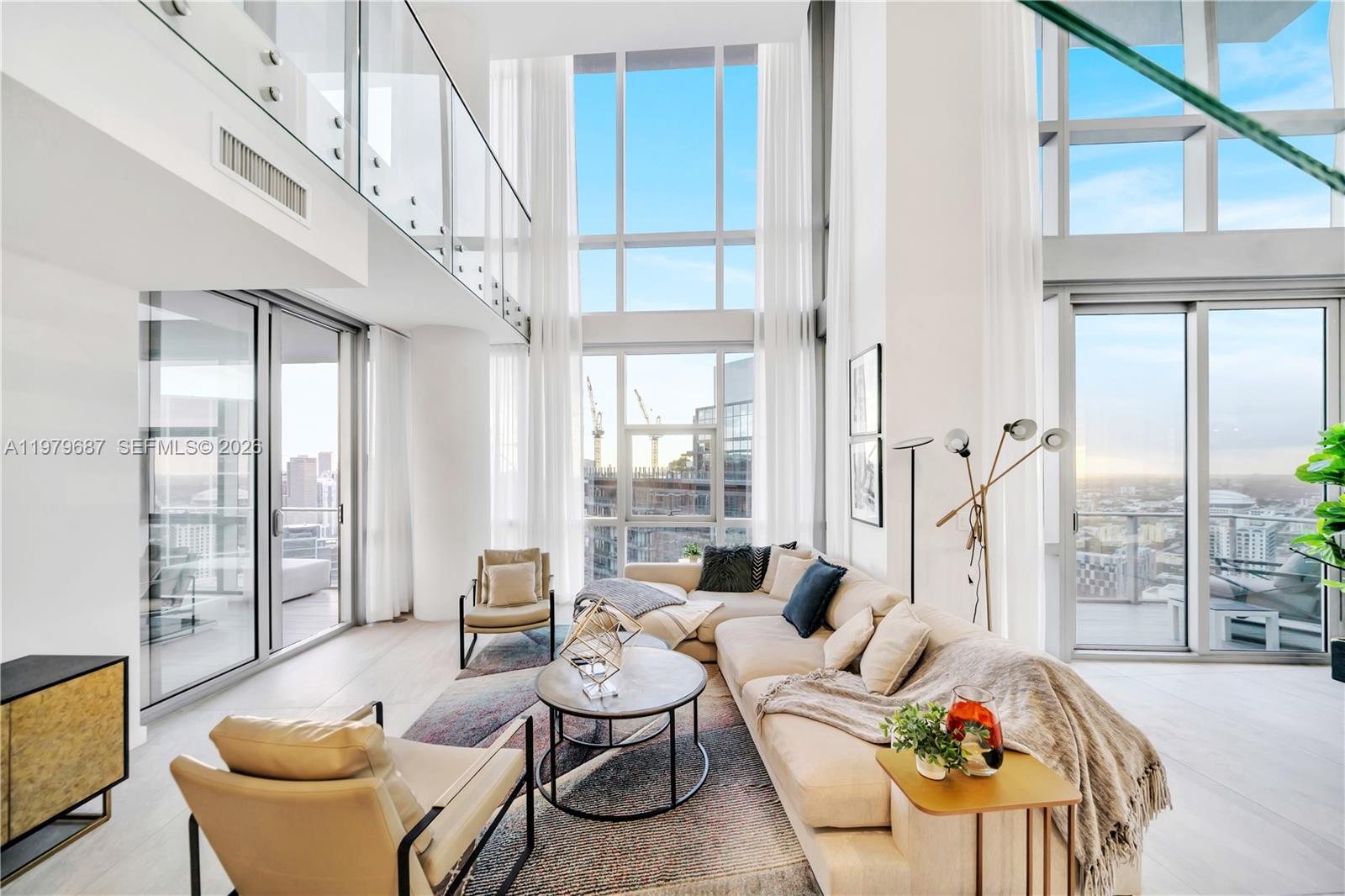 A modern living room features double-height windows, a sectional sofa, and a glass-railed mezzanine balcony — 851 NE 1st Avenue # 4612, Miami FL 33132, MIAMI, FL