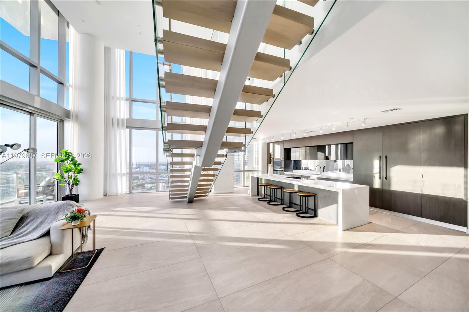 A modern, open-concept living area features a floating staircase, floor-to-ceiling windows, and a sleek kitchen — 851 NE 1st Avenue # 4612, Miami FL 33132, MIAMI, FL