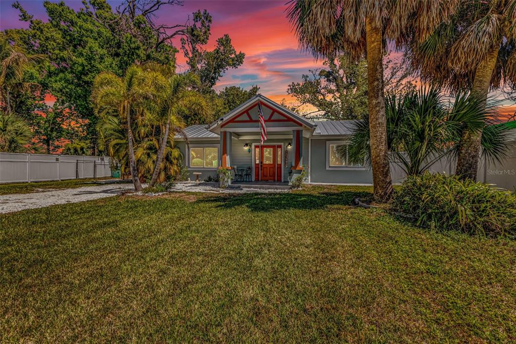 A single-story house with a red-trimmed porch and American flag stands behind a grassy lawn — 115 WINSON AVENUE, ENGLEWOOD, FL