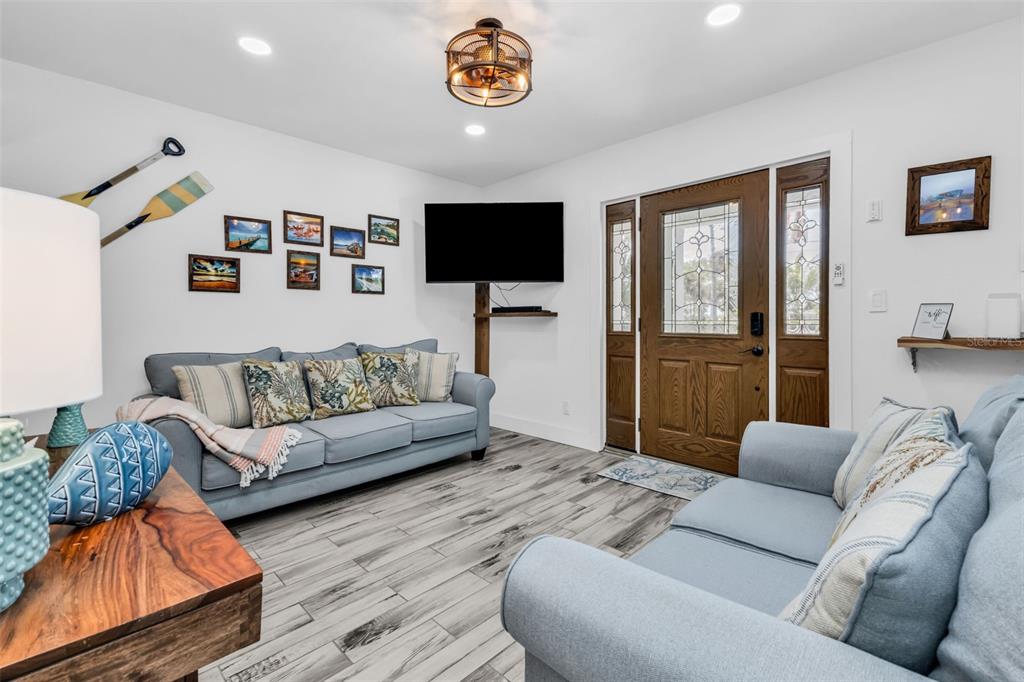A living room features two light blue sofas, a wall-mounted television, and wood-look flooring — 115 WINSON AVENUE, ENGLEWOOD, FL