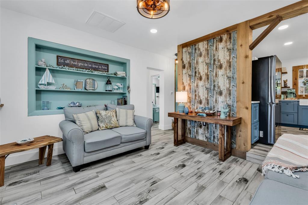 A living room features a blue built-in shelf, a gray sofa, and wood-paneled accent wall — 115 WINSON AVENUE, ENGLEWOOD, FL